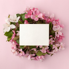 Festive flower apple tree composition and white card with copy space on the pastel pink background. Overhead view
