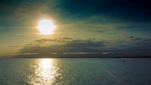 Sunset in the clouds and mountains on the sea in the tourist season with boats and parachute