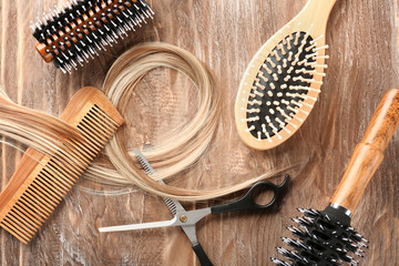 Fototapeta na wymiar Flat lay composition with hairdresser's tools and strand of blonde hair on wooden background