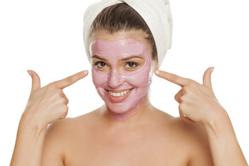 young smiling woman pointing on her facial mask on her face with a towel on her head - Powered by Adobe