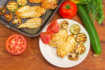 Grilled chicken meat on dish and grill pan, vegetables, greens