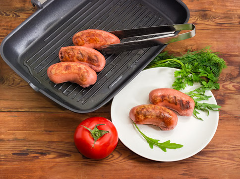Grilled sausages on dish and grill pan, greens and tomato