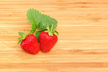 Two garden strawberries with leaf on wooden surface
