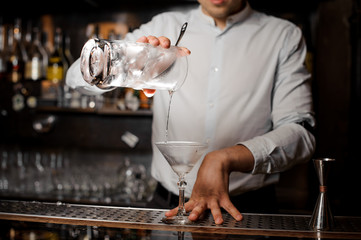Bartender adding an alcoholic drink into the empty cocktail glass