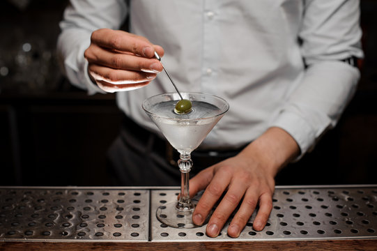 Professional bartender adding an olive into the martini glass