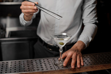 Fototapeta na wymiar Bartender adding an olive into the martini glass with an alcoholic dink