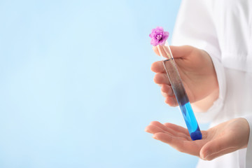 Scientist holding test tube with flowers on color background