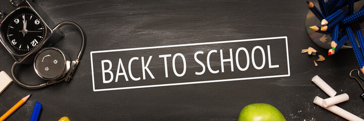 school supplies, alarm, pencils, apple on black chalkboard top view, inscription back to school. long banner