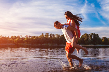 Young man and woman running on summer river bank. Couple having fun at sunset. Guys chilling © maryviolet