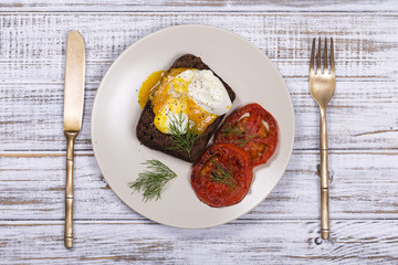 Poached egg on a piece of bread with fried red tomatoes, close up