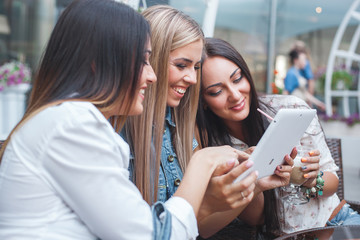 Group of young cheerful women looking at laptop and making online shopping outdoors