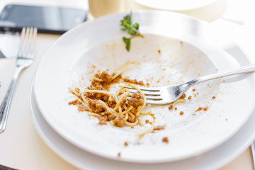 Uneaten residues of meal on the plate. Hungry woman eating tasty pasta. Dish of spaghetti Bolognese