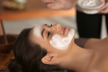 Beautician applying cosmetic mask on woman's face in spa salon