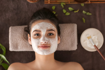 Young woman with face mask relaxing on massage table at spa salon, top view