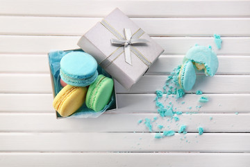 Gift box and tasty macarons on wooden background, top view