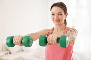 Beautiful young woman doing exercises with dumbbells in morning