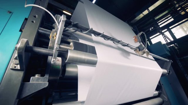 Paper production factory. Printing device rolls paper, close up.