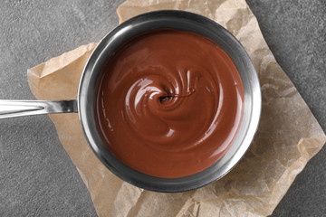 Bowl with tasty melted chocolate on grey table, top view