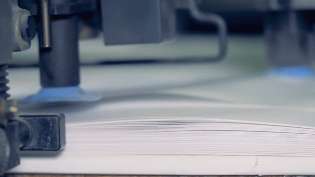 Metal device splits paper at a print factory, close up. Row paper sorting process.