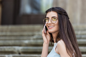 young smiling woman in eyeglasses talking on smartphone on street