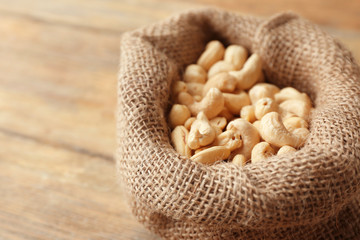 Sack with tasty cashew nuts on wooden table, closeup