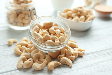 Glass bowl with tasty cashew nuts on light wooden background