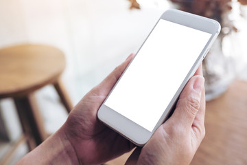 Mockup image of hands holding white mobile phone with blank desktop screen in cafe