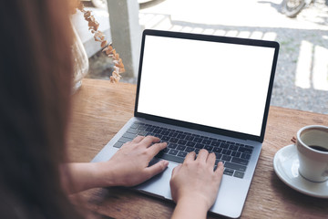 Mockup image of a woman using laptop with blank white desktop screen with coffee cup on wooden table in cafe