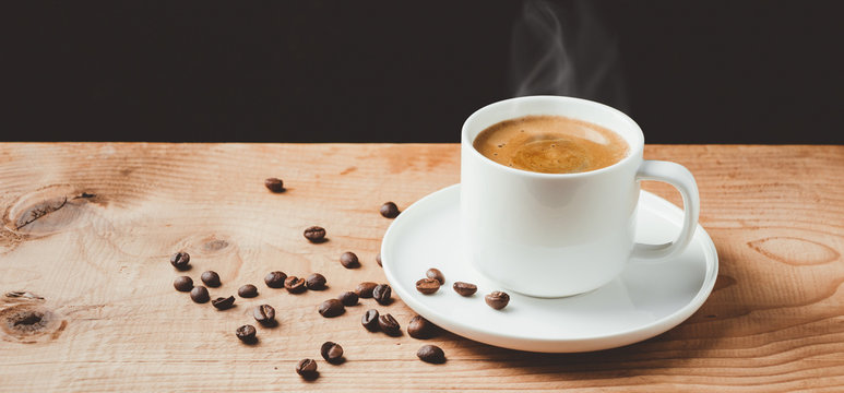 Steaming coffee cup on wooden table with dark background