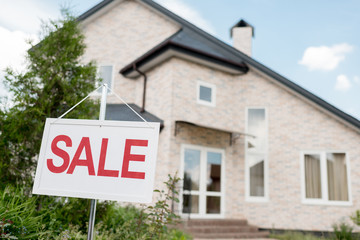 Fototapeta premium close up shot of wooden placard with sale sign in front of modern cottage