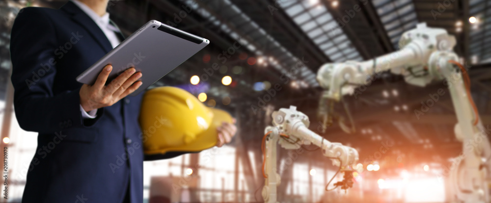 Poster Businessman in a future construction site, Robotics engineer using tablet with control industrial robotics, Automation robot arms machine in intelligent factory industrial. Industry 4.0 concept