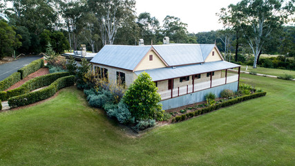 Aerial view of colonial sandstone cottage house with picket fence, garden, grass and eucalyptus gum trees