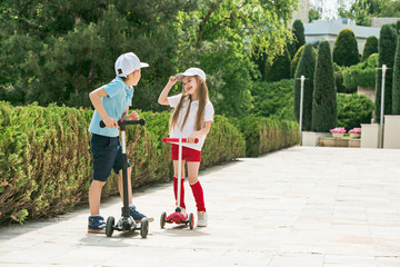 Preschooler girl and boy riding scooter outdoors.