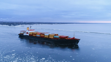 Aerial Shot of the Cargo Ship Moving Through the Sea. In the Background Winter Landscape.