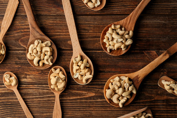 Spoons with tasty cashew nuts on wooden table, top view