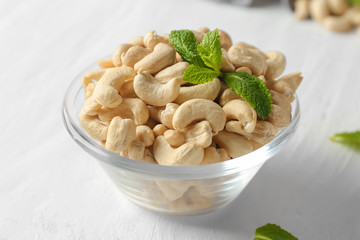 Bowl with tasty cashew nuts on white wooden background