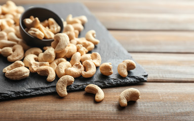 Slate plate and tasty cashew nuts on wooden background