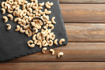 Obraz na płótnie Canvas Slate plate and tasty cashew nuts on wooden background