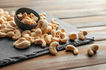 Slate plate and tasty cashew nuts on wooden background
