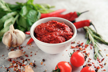 Bowl with red sauce and vegetables on grey background