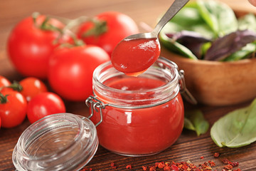Glass jar and spoon with red sauce, closeup