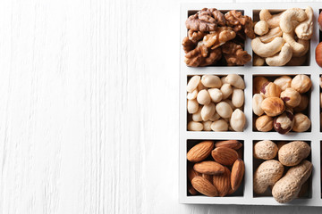 Box with different nuts on white wooden background