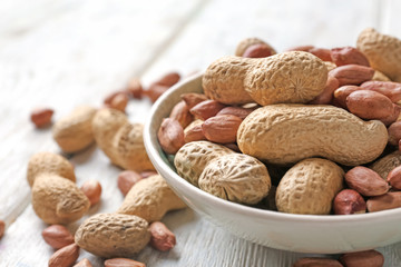 Bowl with peanuts on wooden table, closeup