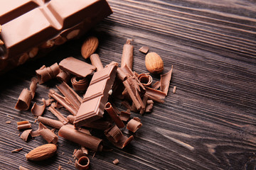 Chocolate bar with curls and almonds on wooden table