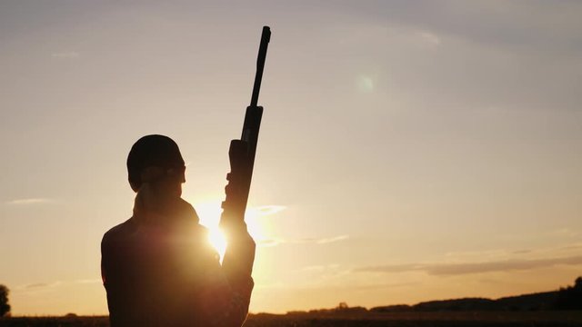 Silhouette of a woman with a rifle in the rays of a sunset. Sports shooting