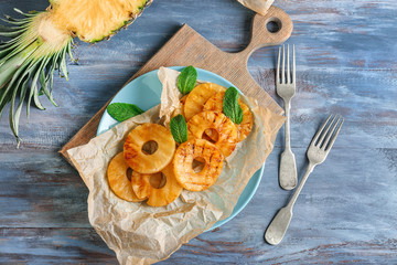 Plate with grilled pineapple slices on wooden table