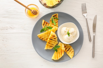 Plate with grilled pineapple slices and ice cream on wooden table