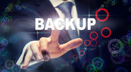 A businessman pressing a Backup business concept on a graphical display of cogs