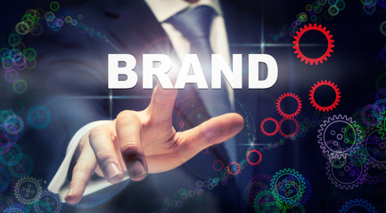 A businessman pressing a Brand business concept on a graphical display of cogs