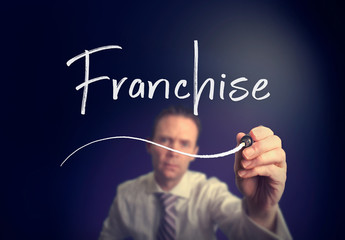 A businessman writing a Franchise concept with a white pen on a clear screen.
